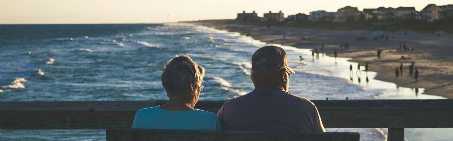 Retired couple sitting on bench looking at ocean.